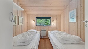Ett rum med två separata sängar, ett fönster med utsikt över träd och en väggmonterad lampa.