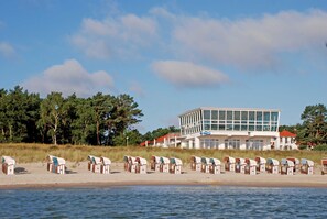Un edificio frente al mar con diseño moderno, una hilera de cabañas de playa y vistas al océano.