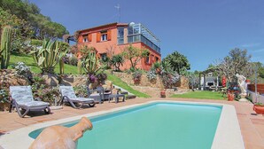 A swimming pool with lounge chairs, a stone wall, and a building with a red facade and a glass balcony. - Beautiful apartment in Palamós (Palamós)