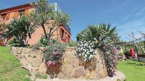 A stone wall with flowers and plants, a building with a red facade, and a clear blue sky. - Beautiful apartment in Palamós (Palamós)