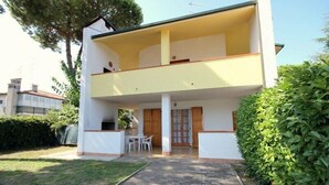 A two-story building with a balcony on the upper floor, a small outdoor seating area, and a paved entrance. - Holiday home with garden, terrace and barbecue facilities (Lido delle Nazioni)