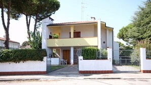 A two-story residential building with a balcony, a gated entrance, and a small patio area. - Holiday home with garden, terrace and barbecue facilities (Lido delle Nazioni)