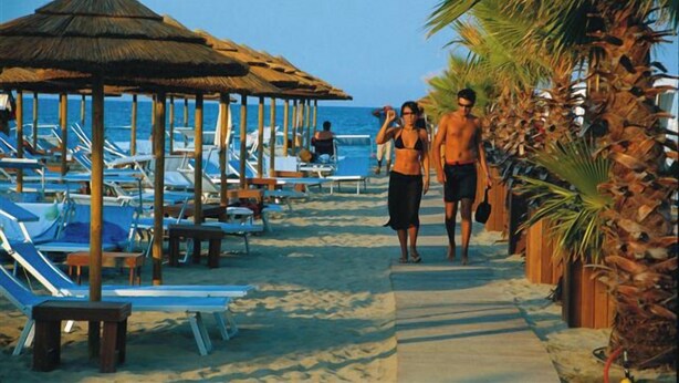 A beach with sun loungers, a thatched-roof structure, and palm trees. - Holiday home with garden, terrace and barbecue facilities (Lido delle Nazioni)