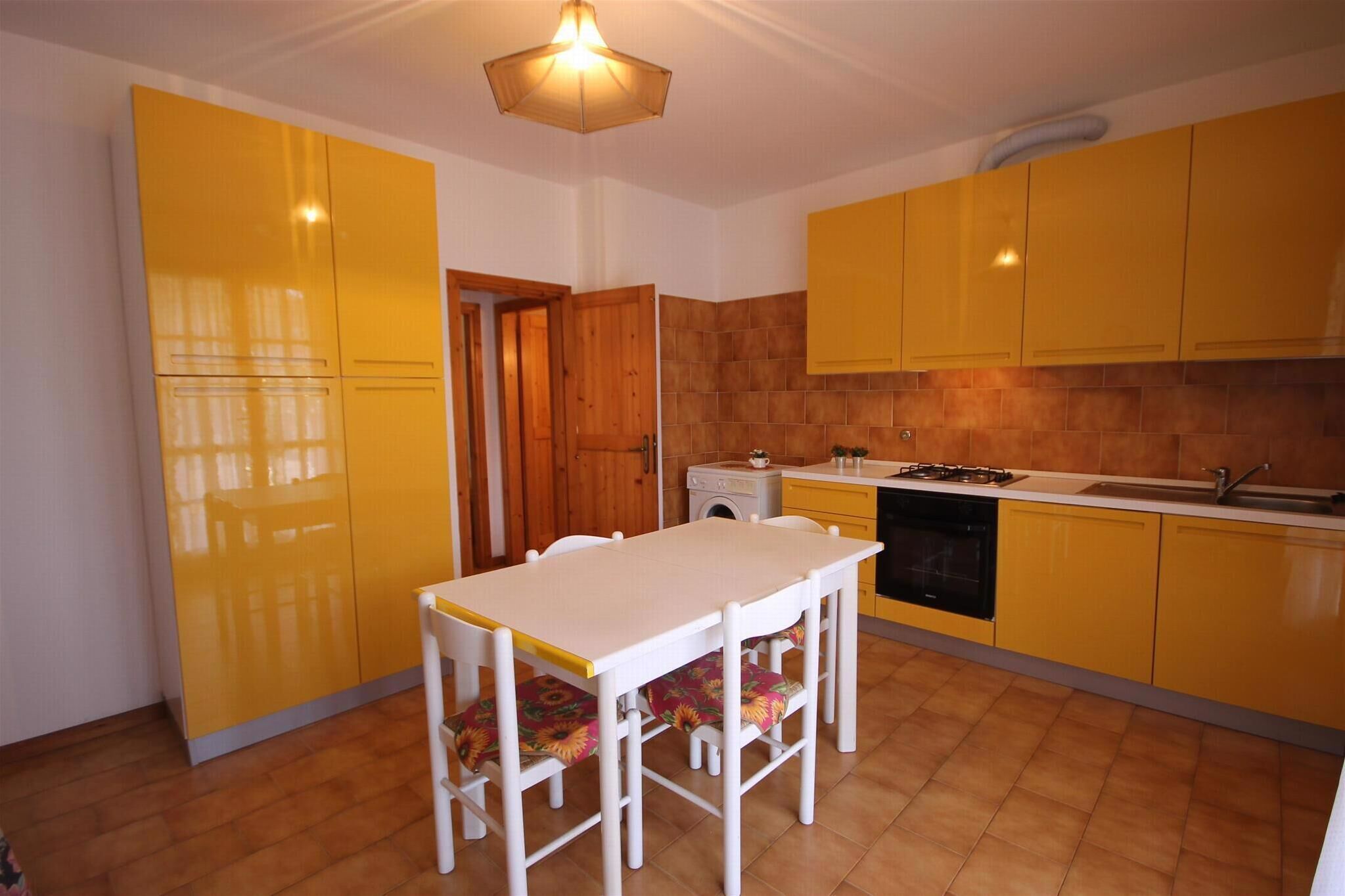Une cuisine avec des meubles de couleur jaune, une table blanche et une porte en bois.
