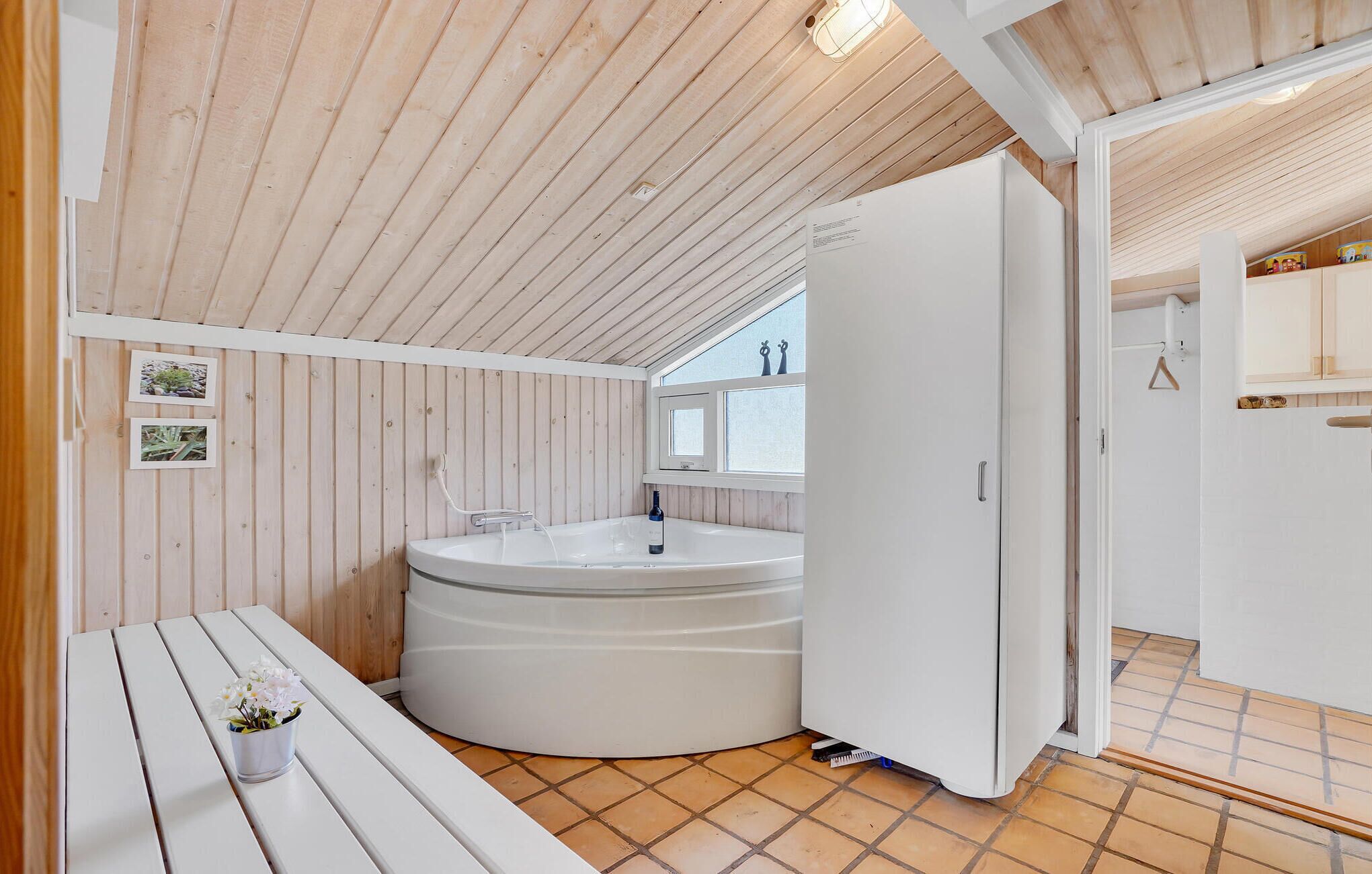 A modern bathroom with a freestanding bathtub, wooden walls, a window, and a white door.