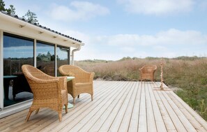 Una terraza de madera con sillas de mimbre y una mesa, con vistas a un paisaje natural.