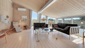 Een ruime woonkamer met een houten vloer, een zwarte bank, een gestreept fauteuil en een glazen salontafel.