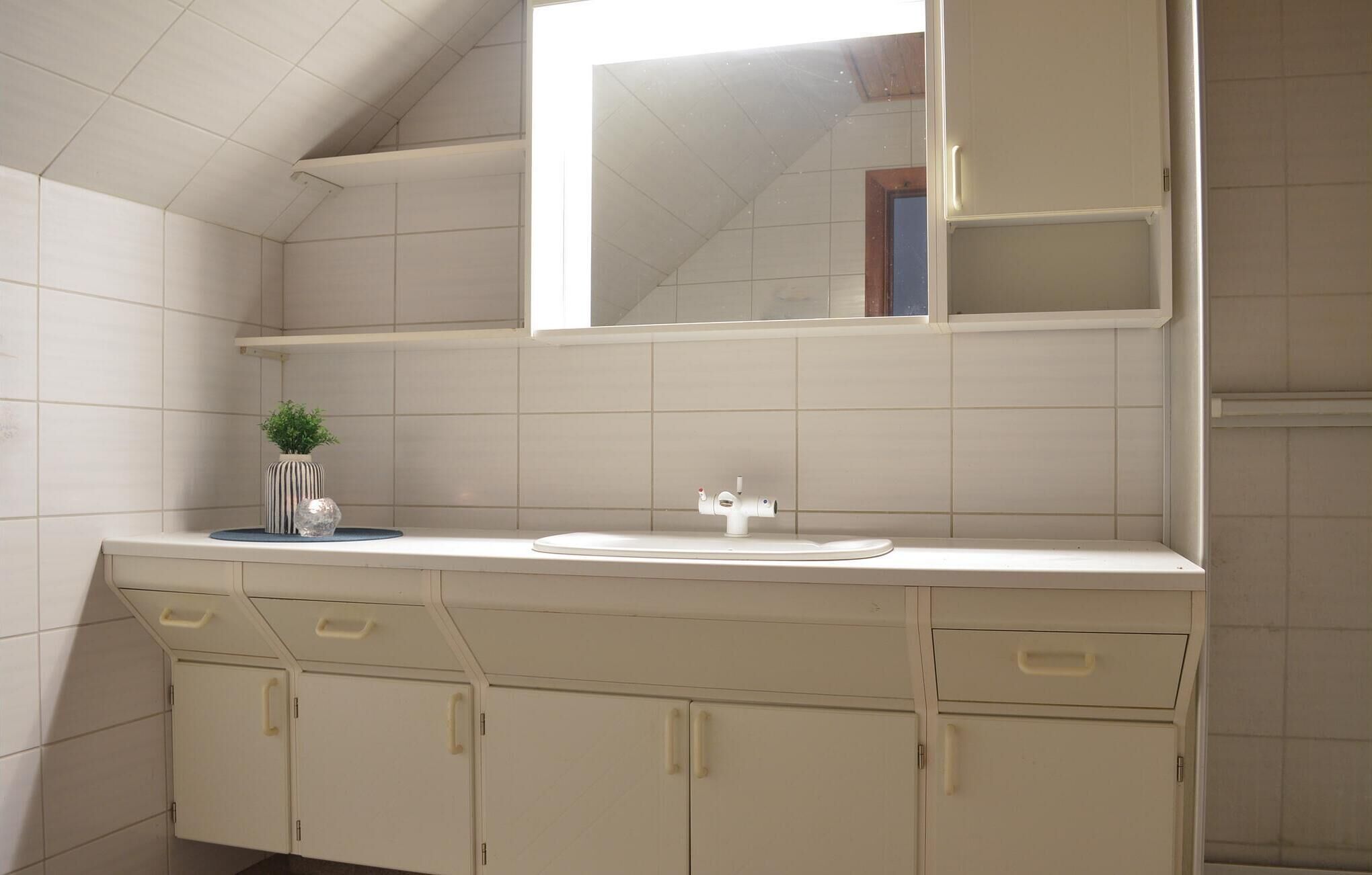 Une salle de bain avec un meuble-lavabo blanc, un miroir et une petite plante en pot.