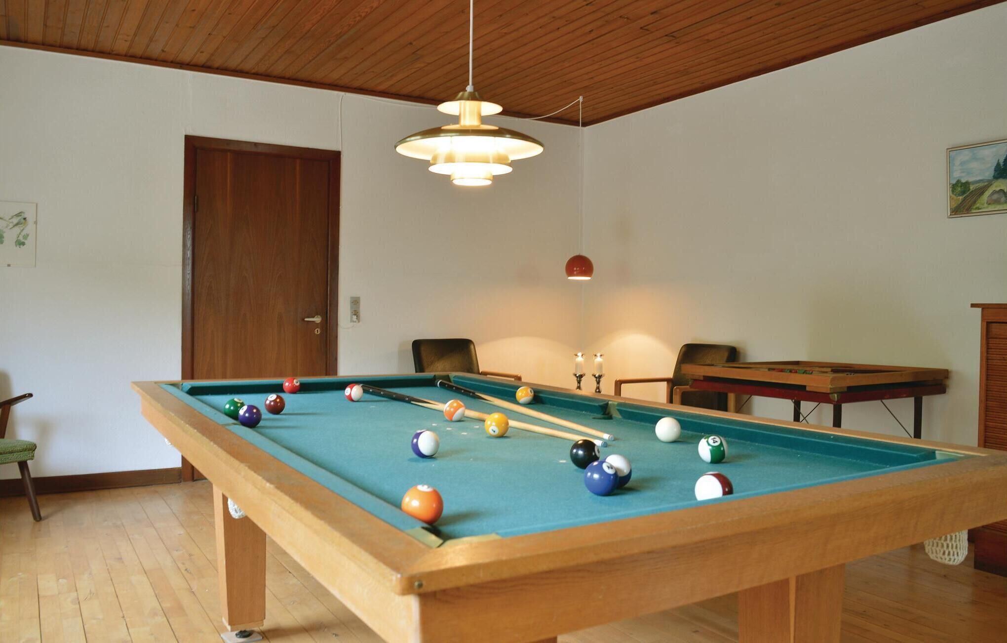 A pool table with balls, a wooden ceiling, a door, and a painting on the wall.