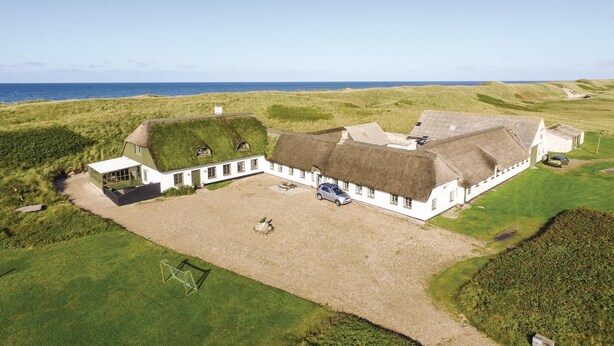 Ein traditionelles weißes Gebäude mit einem Reetdach, umgeben von grünen Feldern und Blick auf das Meer.