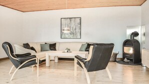Ein modernes Wohnzimmer mit Holzboden, einem beigen Sofa, zwei schwarzen Ledersesseln, einem weißen Couchtisch und einem Kamin.