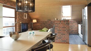 Una cocina moderna con pared de ladrillo, una isla grande con sillas, un colgante de luz y un televisor sobre un mueble.