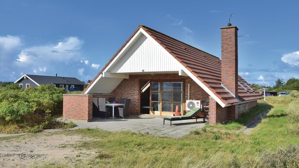 Una casa de un piso con techo inclinado, una chimenea de ladrillo y un patio con mobiliario exterior.