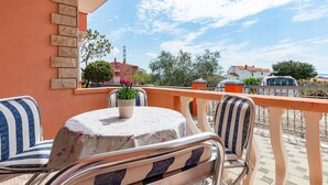 A balcony with a round table and two chairs, a potted plant, and a view of the street and buildings in the background. - Nice apartment in Betiga with WiFi (Betiga)