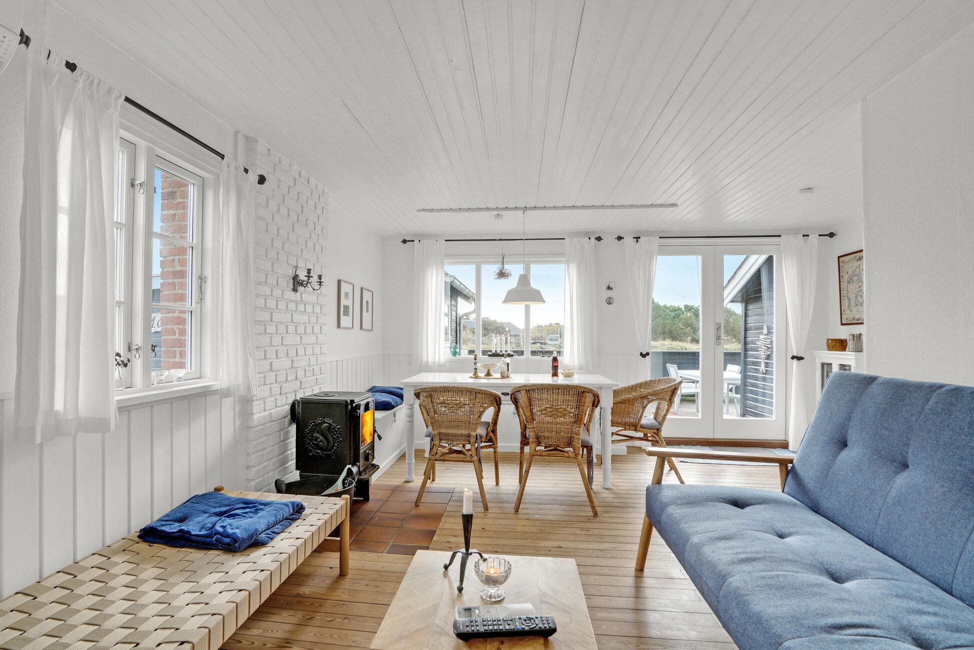 A bright, open-plan living space with a fireplace, wicker furniture, and a blue sofa.