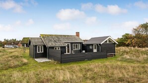 Ein schwarzes Holzhaus mit Strohdach, Schornstein und einer kleinen Veranda.