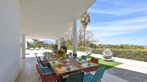 Un espace de restauration en plein air avec une table en bois, des chaises colorées et une vue sur une piscine et des montagnes.