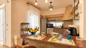 Une cuisine dotée de plans de travail en granit, un coin repas avec des chaises, une machine à café et un panier de fruits.