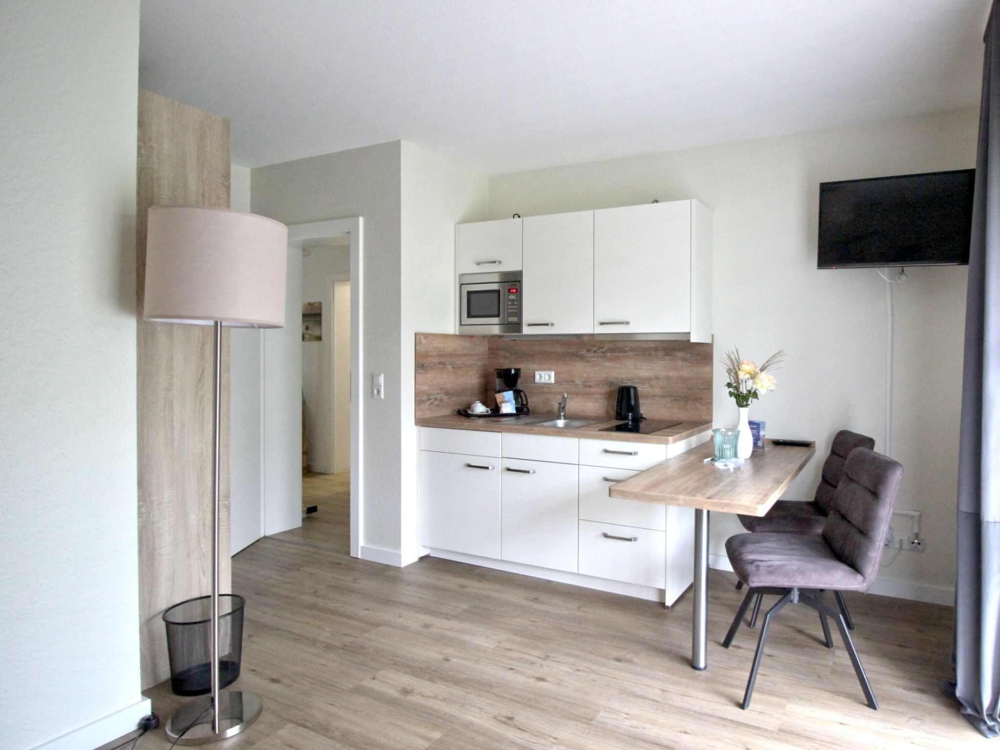 Eine moderne Küche mit weißen Schränken, einer Holz Arbeitsplatte und einer eingebauten Mikrowelle. Es gibt einen Essbereich mit Tisch und Stühlen sowie einen an der Wand montierten Fernseher.