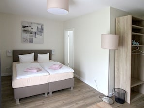 A bedroom with a bed, a bedside table, a lamp, and a wardrobe.