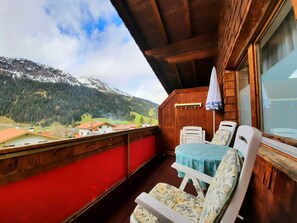 A balcony with a table and chairs, a wooden wall, and a view of mountains and houses.