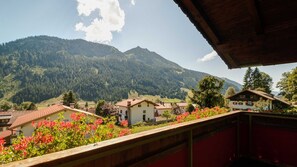A mountain village with traditional houses, a wooden balcony, and a view of the surrounding hills.
