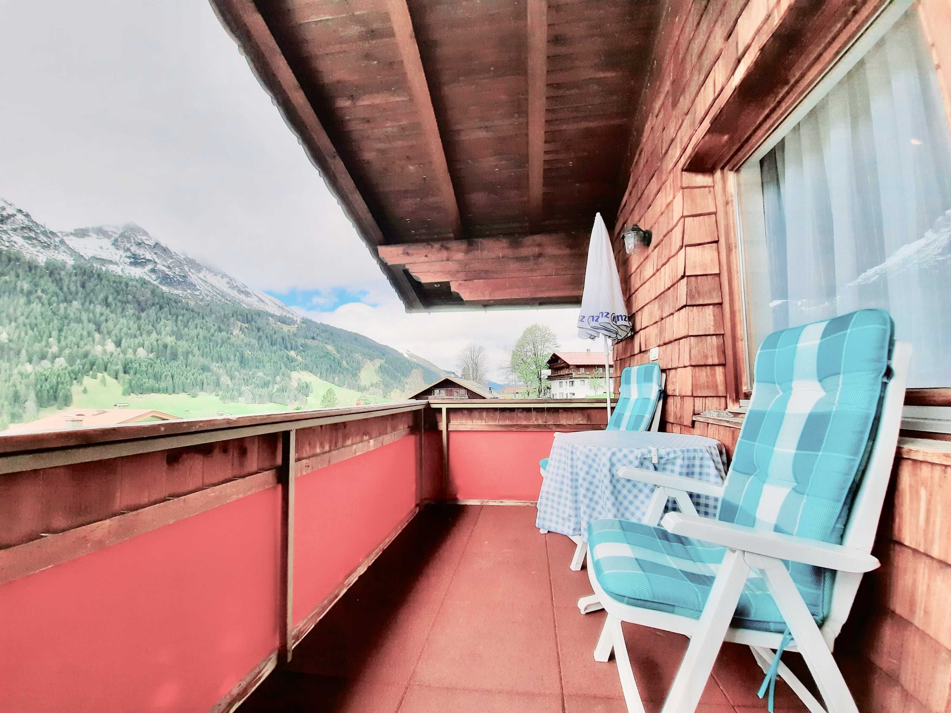A balcony with wooden railings, a table with a checkered tablecloth, and two checkered chairs.