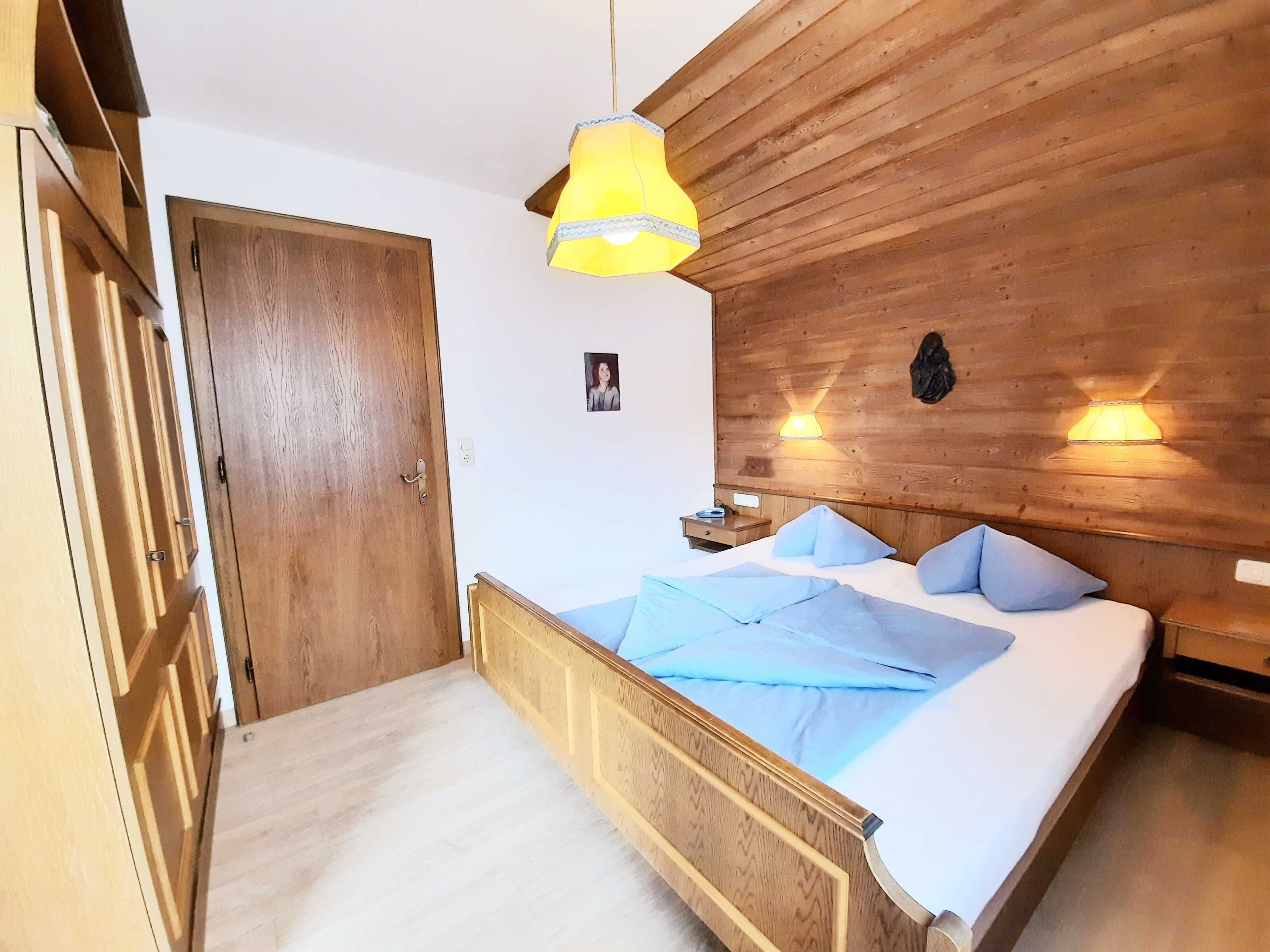 A wooden-paneled room with a bed, a hanging light fixture, and a wall-mounted lamp.