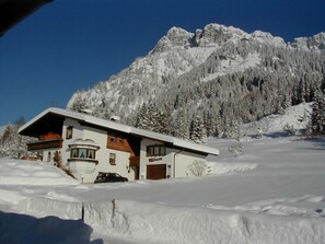 A snow-covered mountain with a chalet-style house in the foreground.