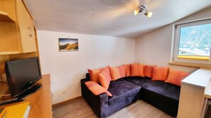 Un espacio habitable compacto con un sofá modular, una televisión, una ventana con vistas y una lámpara de techo.