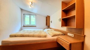 Un dormitorio con dos camas, una ventana, un armario de madera y una mesita de noche.
