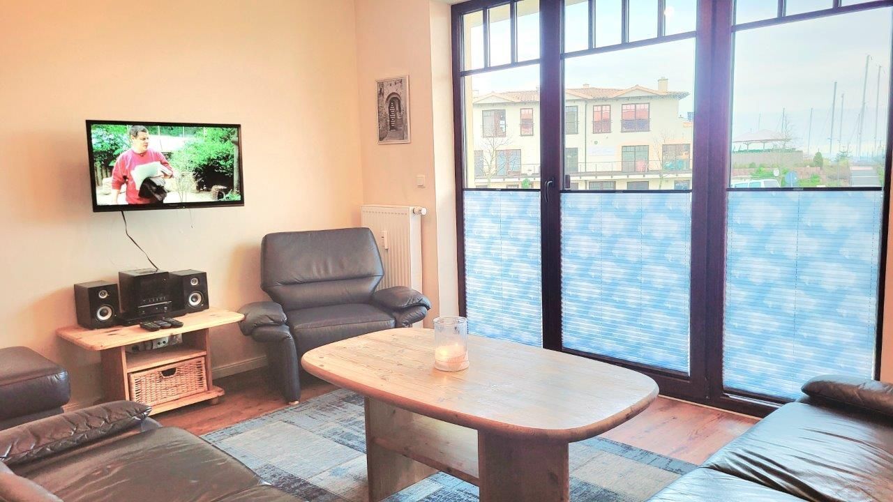 A living room with a television, a leather chair, a wooden coffee table, and a view of a building through large windows.
