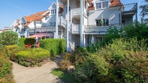 A multi-story residential building with balconies, a covered walkway, and a garden area.