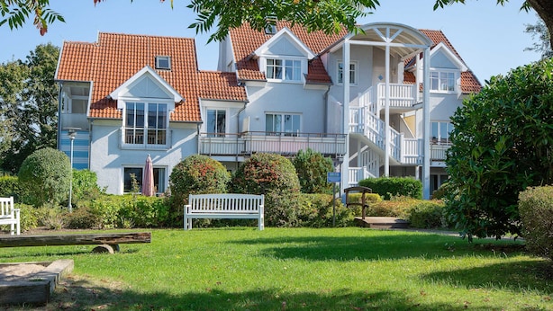 A multi-story building with a red-tiled roof, white exterior walls, and a central staircase leading to a balcony.