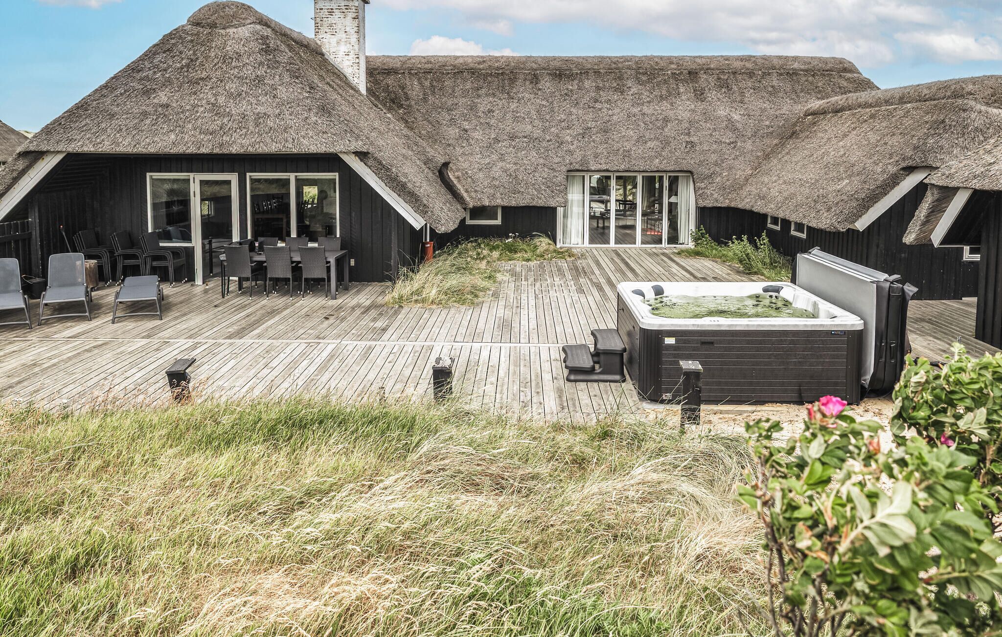 A thatched-roof building with a wooden deck and a hot tub.
