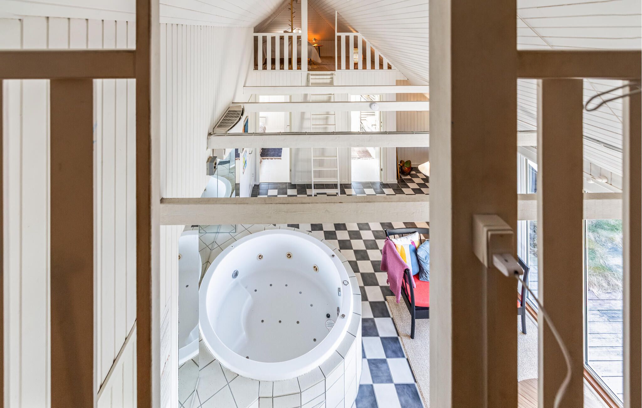 Ein mehrgeschossiges Interieur mit einem Schachbrettmuster-Boden, einer großen Badewanne und einer Treppe.