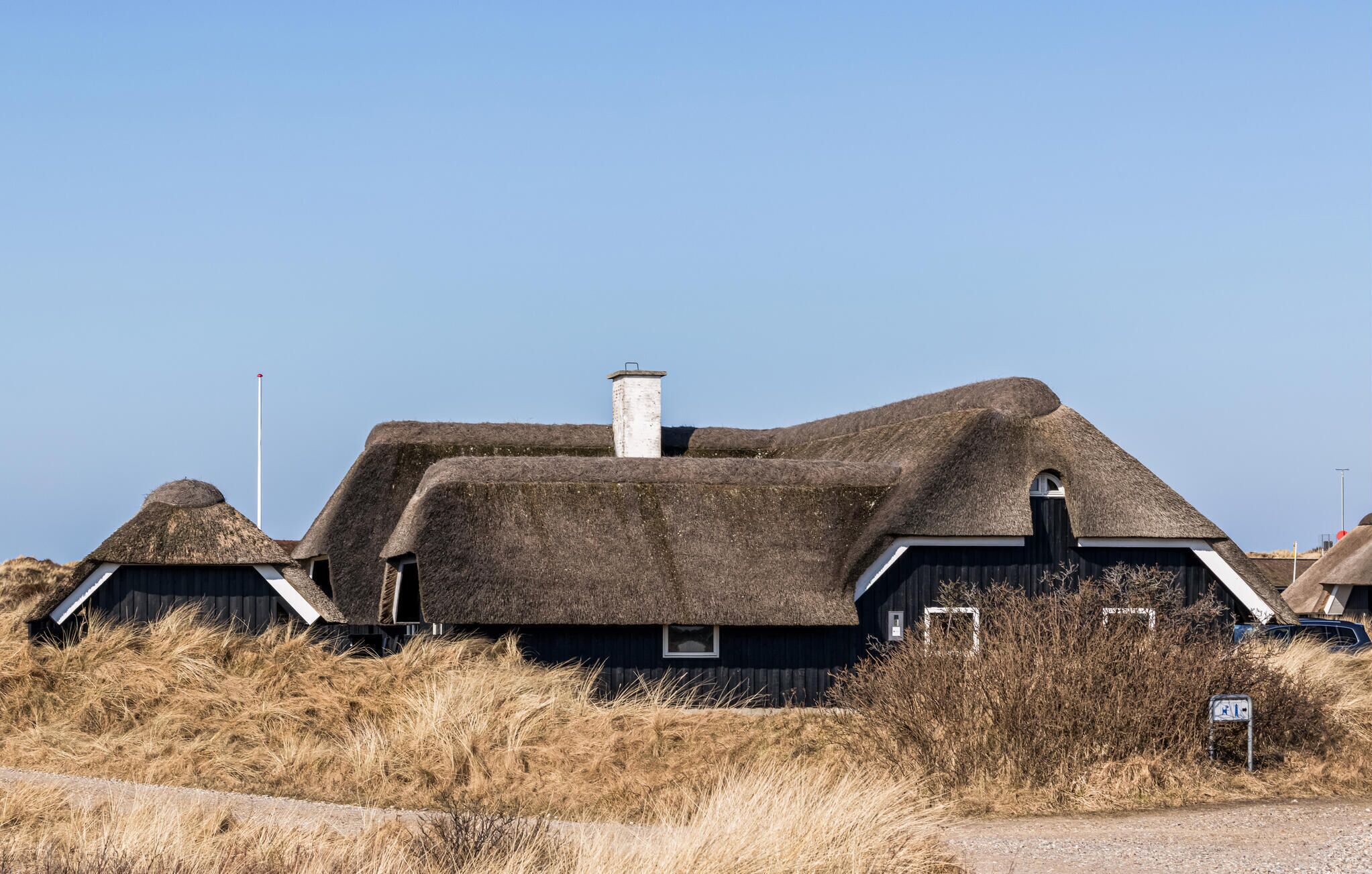 Een traditioneel rieten huis met schoorsteen, omgeven door droog gras en een heldere lucht.