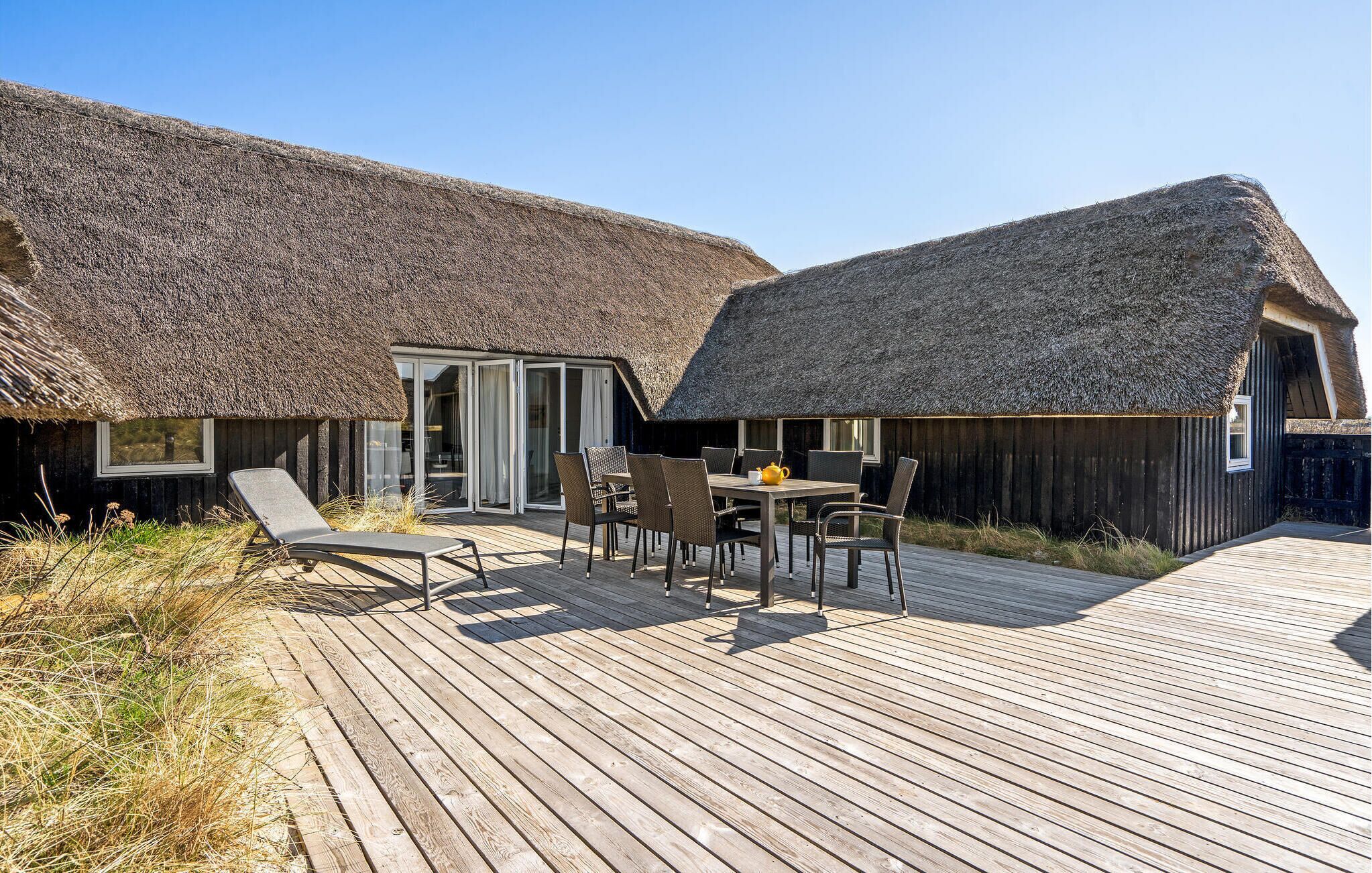 Un bâtiment à toit de chaume doté d’une terrasse en bois et d’un espace extérieur aménagé pour s’asseoir.