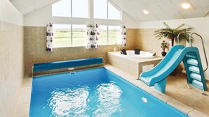 Una piscina con un tobogán azul, un jacuzzi y vistas al exterior a través de amplios ventanales.