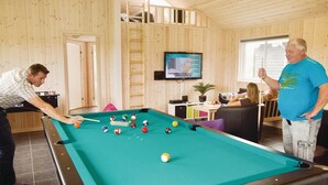 Una mesa de billar en una habitación con paredes de madera y un televisor montado encima.