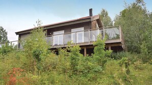 Ett tvåvåningshus i trä med en balkong, omgivet av tät vegetation.