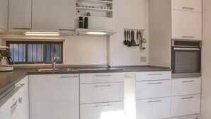 Una cocina moderna con armarios blancos, horno empotrado y pileta de acero inoxidable.
