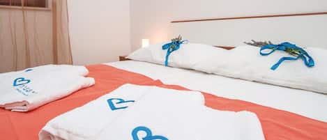 A hotel room with a bed, two white towels with a blue heart logo, and a window with blinds.