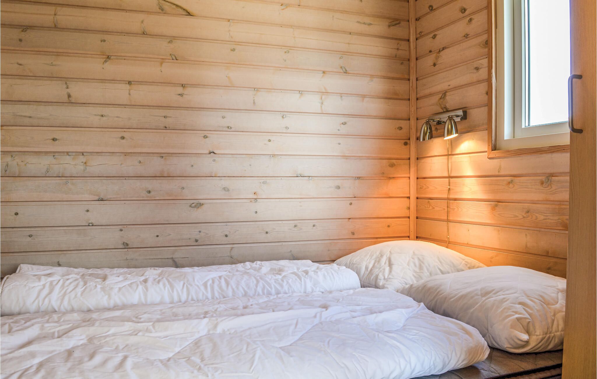 A small, cozy room with wooden walls and a single bed with white bedding.