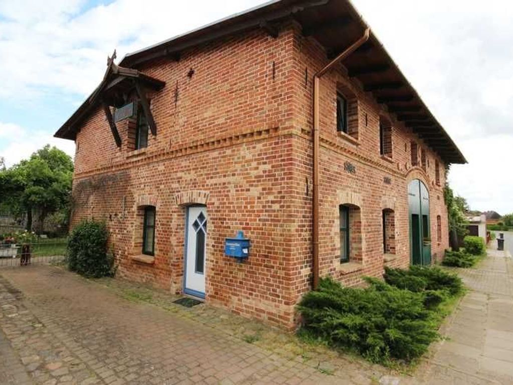 A brick building with a gabled roof, a small porch, and a door with a window above it.