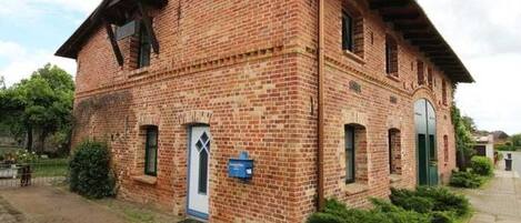 A brick building with a gabled roof, a small porch, and a door with a window above it.
