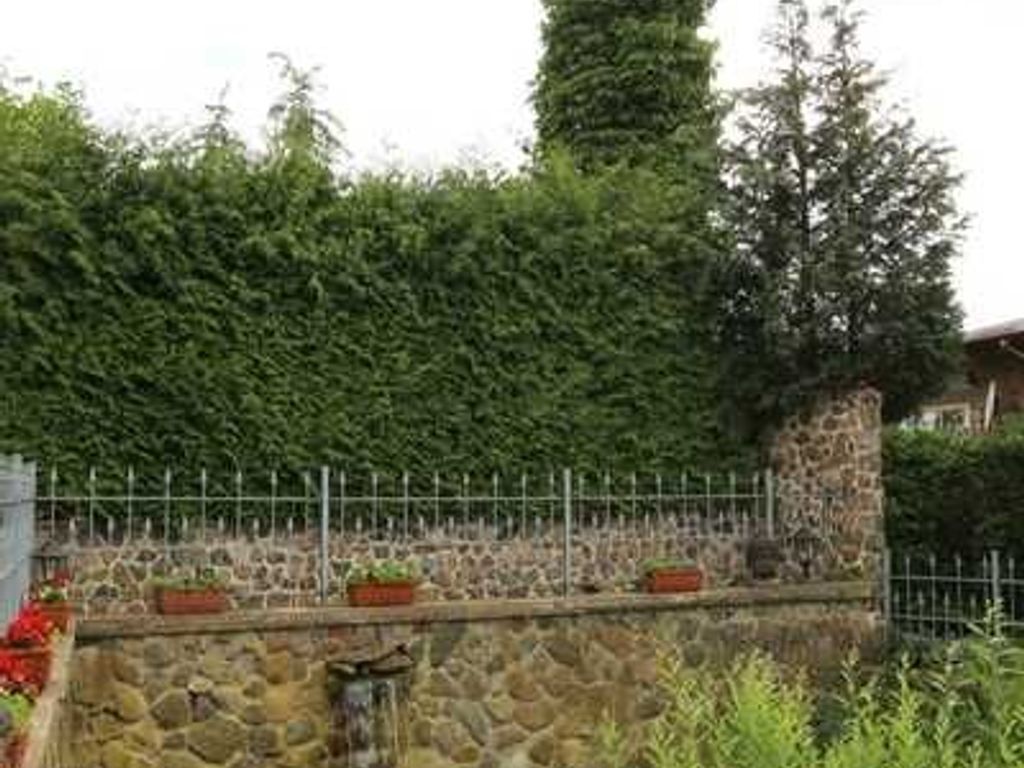 A stone wall with a metal fence, potted plants, and a stone structure.