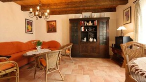 A cozy living room with a wooden ceiling, a sofa, wicker chairs, a table, and a cabinet with decorative items. - Apartment 1 - Fewos "Storchenhof" near the lake (Meesiger)