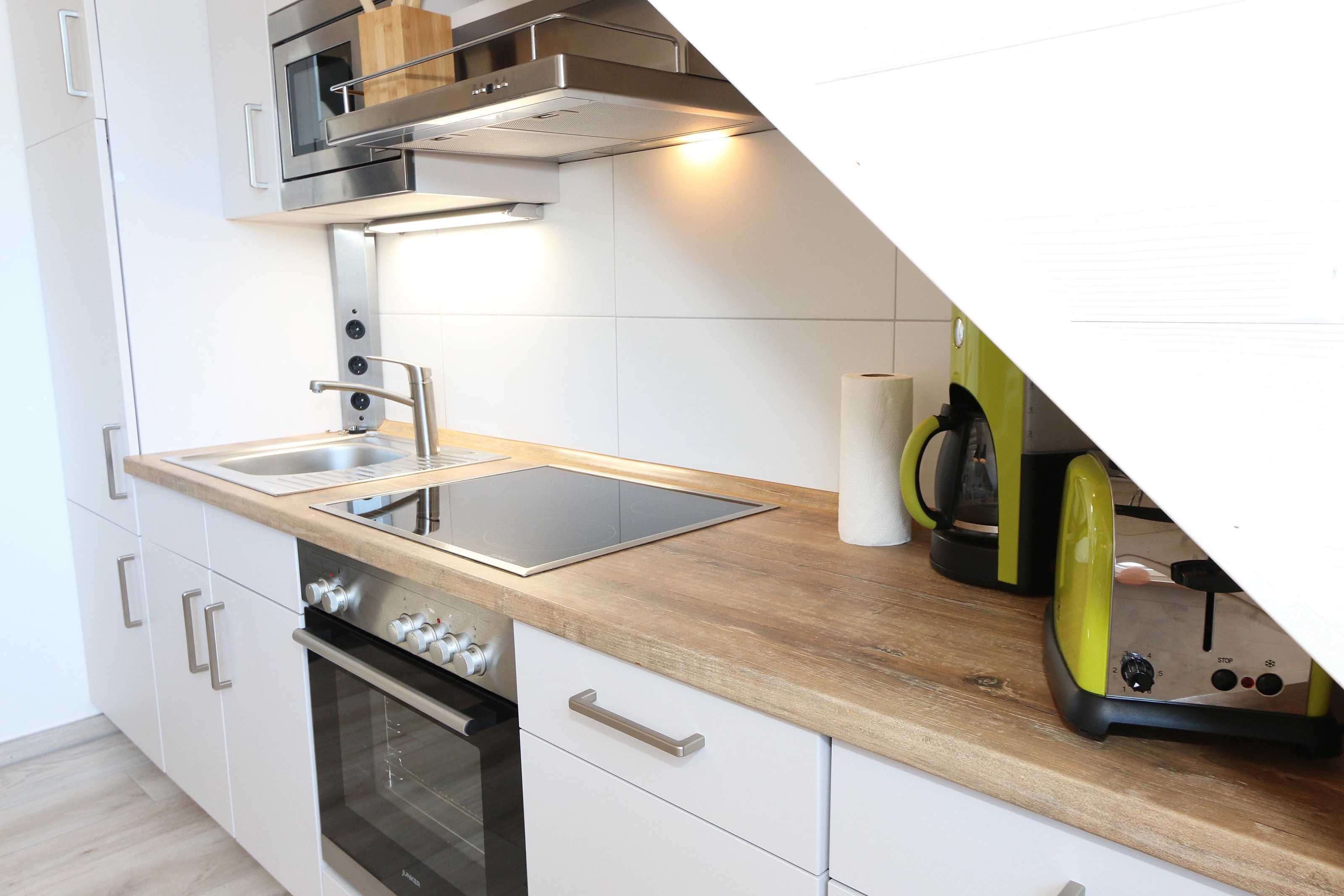 A modern kitchen with a built-in oven, a stainless steel range hood, and a wooden countertop.