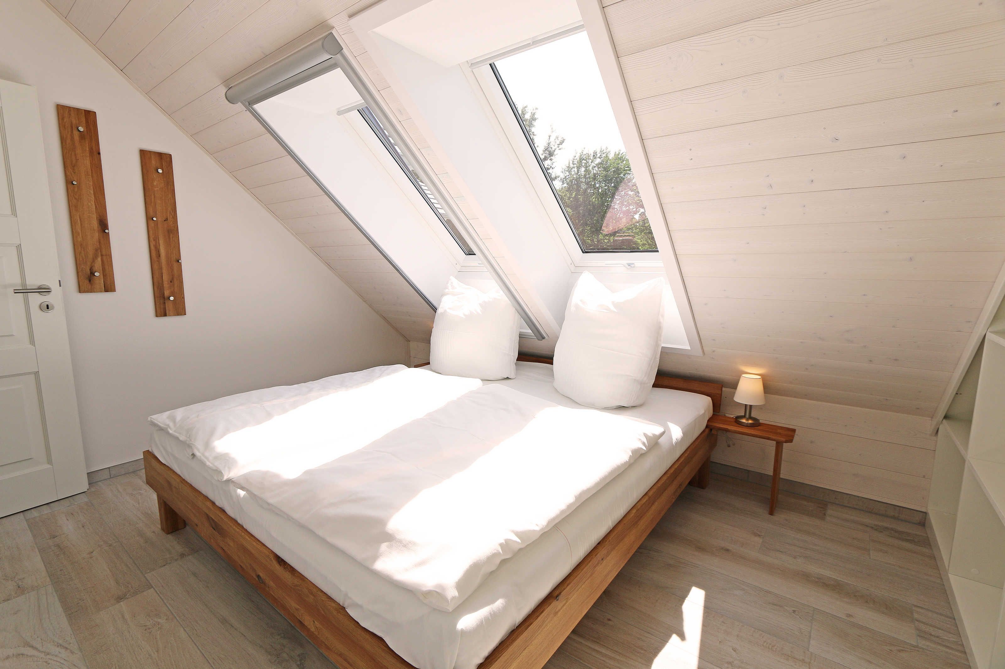 A bedroom with a sloped ceiling, skylights, a wooden bed frame, and a bedside table with a lamp.